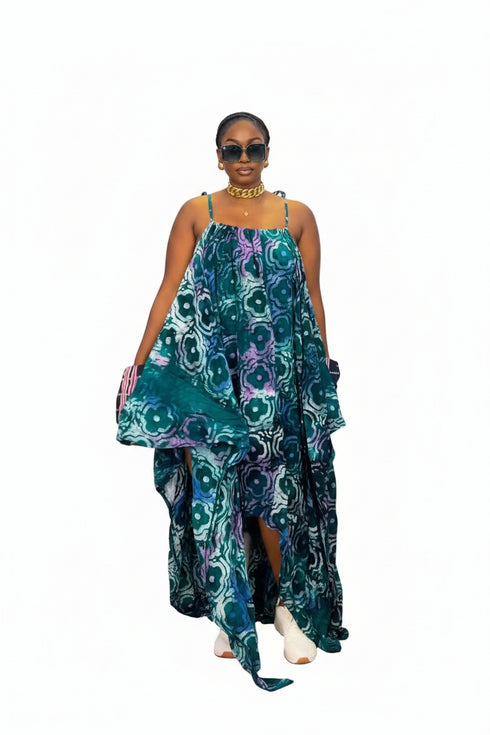 A woman modeling a sleeveless high-low dress with a swirling abstract pattern in teal, green, purple, and white, set against a plain white background.