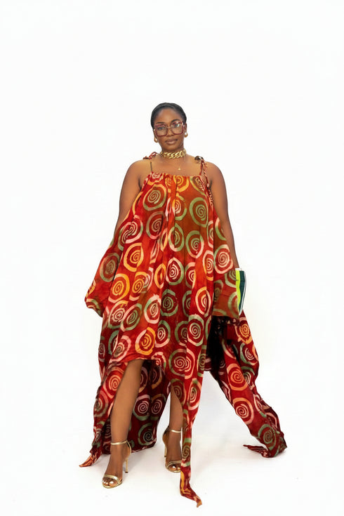 A woman modeling a vibrant red halter dress with a bold circular pattern in orange, yellow, green, and brown, styled with white sneakers against a plain white background.