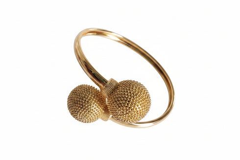 Gold bangle with textured spherical ends on a marble surface
