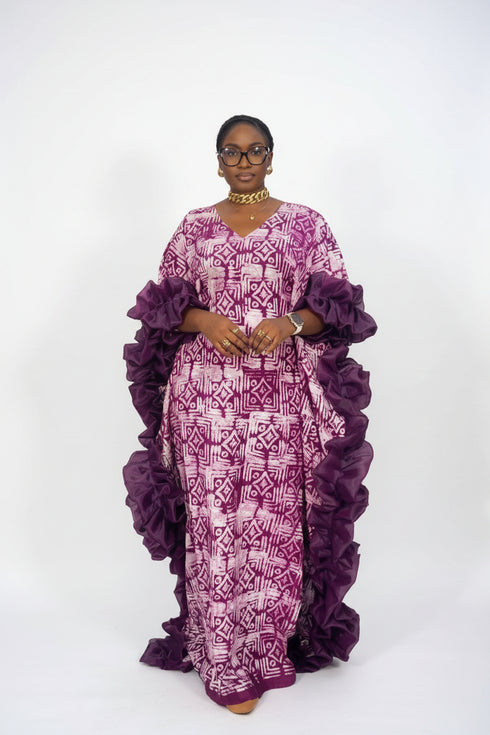 A woman modeling a purple and pink patterned traditional dress with voluminous ruffled sleeves, shown in a social media post with text overlays indicating the price and WhatsApp contact.