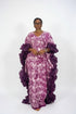 A woman modeling a purple and pink patterned traditional dress with voluminous ruffled sleeves, shown in a social media post with text overlays indicating the price and WhatsApp contact.