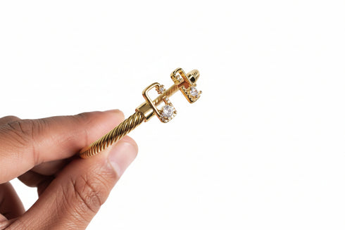 Gold bracelet with a textured design held by a hand against a marble background