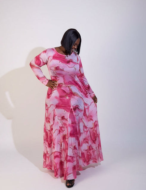A woman modeling a long-sleeve maxi dress with a pink and white marble pattern, standing against a plain white studio background.