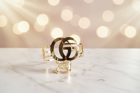 Gold bracelet with a logo on a marble surface with a bokeh light background