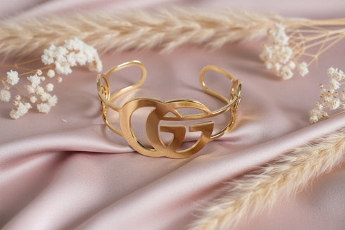 Gold bracelet with a unique design on a pink fabric background with dried flowers and grasses.