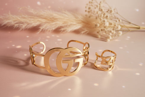 Gold bracelet and ring set on a soft pink background with dried flowers.
