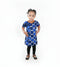 A young child standing in a living room wearing a blue and white patterned dress with orange trim, black leggings, and braids.