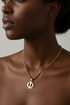 Woman wearing a gold necklace with a pendant on a neutral background