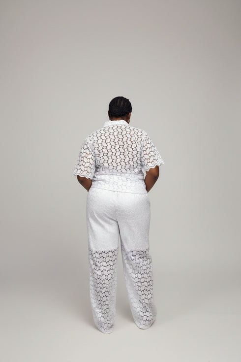 A person shown from behind wearing a white lace outfit with a black geometric patterned top and white pants, standing indoors in front of a black slatted wall. Large overlaid text at the top reads 'Price - N40,000 WhatsApp +2347030500842', and social-style interface icons and a phone preview are visible around the frame.