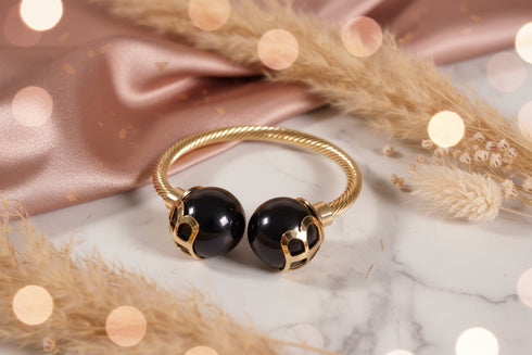 Gold bracelet with black beads on a marble surface