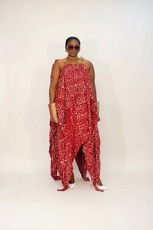 A woman modeling a red and white abstract patterned maxi dress with side cutouts, standing in front of a modern black and white striped wall.