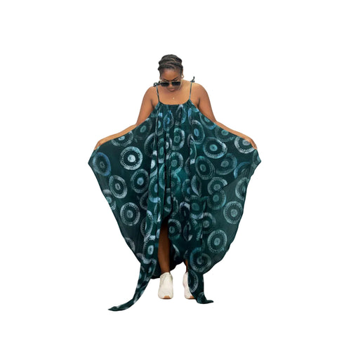 A woman modeling a dark teal green halter dress with a white circular mandala pattern, holding the wide sleeves out to the sides against a solid white background.