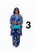 A woman modeling a blue and white floral print kaftan outfit with matching trousers, holding a bright turquoise handbag, and wearing blue-tinted sunglasses against a solid white background.