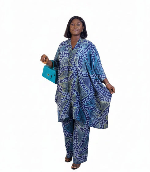 A woman modeling a matching blue and white patterned kaftan tunic and trouser set, holding a bright turquoise handbag against a plain white background.