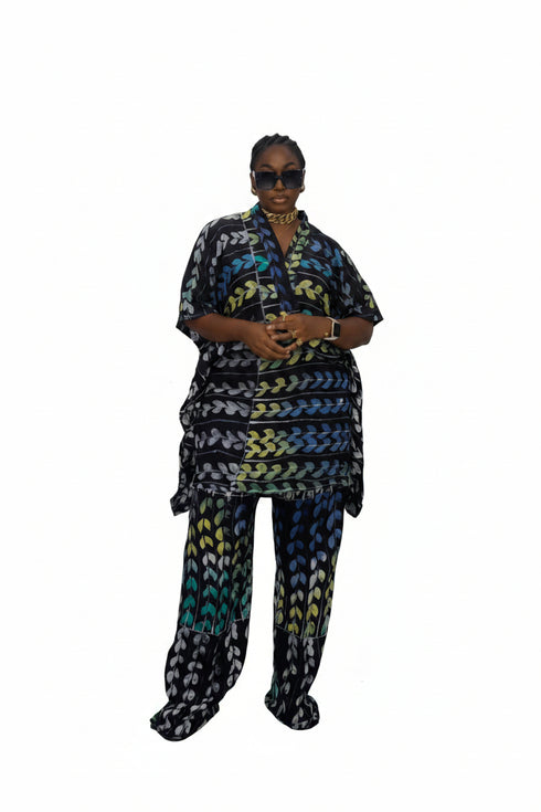 A person wearing a matching two-piece patterned outfit with a black, blue, green, and yellow abstract design, standing in front of a black and white paneled wall. A white 'Watch more reels' overlay is on the screen.