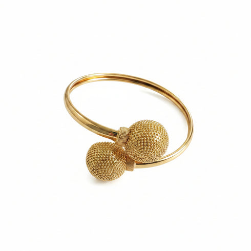 Gold bangle with textured spherical ends on a marble surface