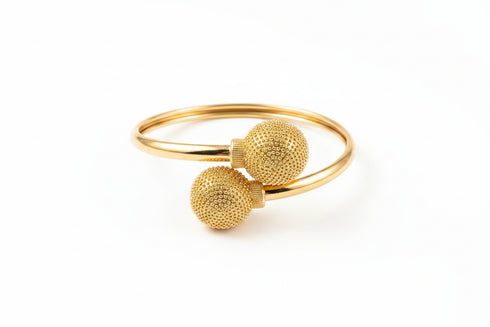 Gold bracelet with textured spherical ends on a marble surface