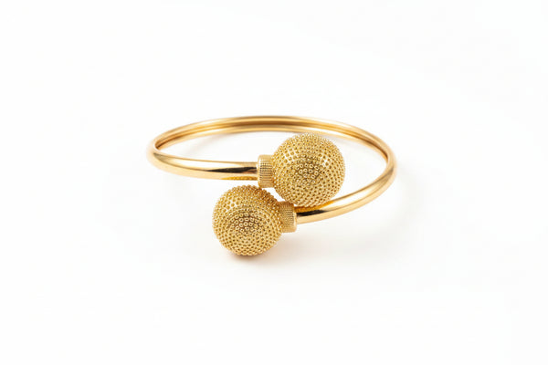 Gold bracelet with textured spherical ends on a marble surface