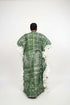 A person viewed from behind wearing a green patterned kaftan dress with wide white ruffled sleeves, standing indoors in front of a black slatted wall. Large text at the top reads 'Readily available Price - N35,000 each WhatsApp +2347035008482', and a small phone screen inset appears at the bottom left.
