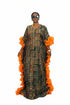 A woman modeling a long, loose-fitting patterned dress with bright orange ruffled sleeve and side details, standing in front of a black-and-white striped wall. The dress has a dark green and beige geometric print.