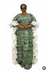 A woman modeling a green and white patterned kaftan dress with dramatic white ruffled sleeves, standing in front of a black and white striped wall.