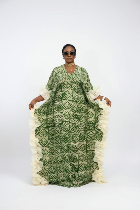A woman modeling a green patterned kaftan dress with white ruffled trim, shown in a social media-style video frame with text overlays and phone interface elements.