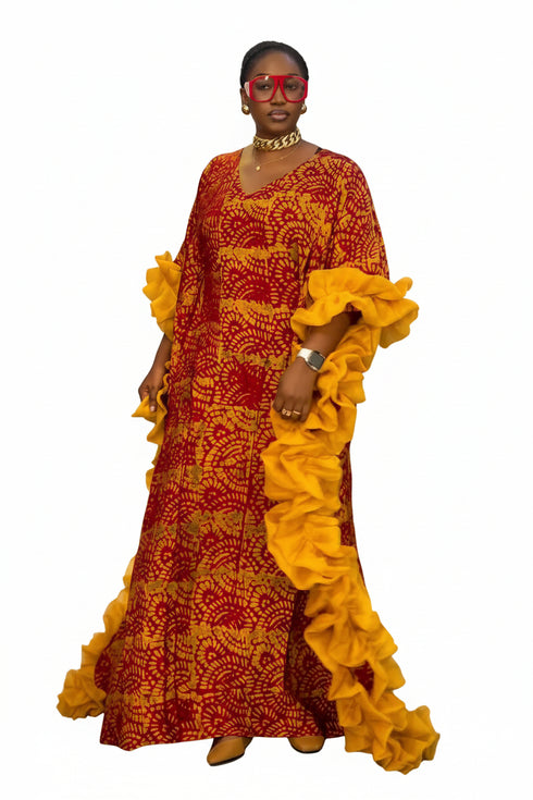 A woman modeling a long red and yellow patterned kaftan dress with dramatic ruffled sleeves, standing in front of a black and white striped wall.