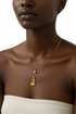 Woman wearing a gold necklace with a heart-shaped pendant on a plain background