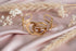 Gold bracelet with a unique design on a pink fabric background with dried flowers and grasses.