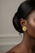 Close-up of a person wearing gold earrings with a neutral background