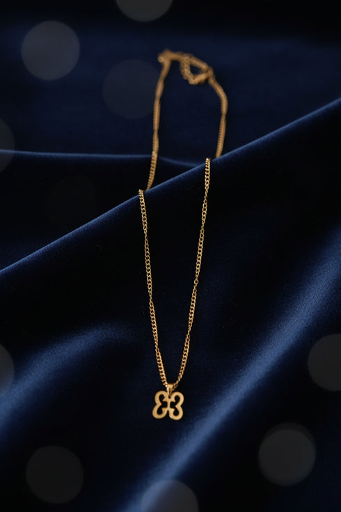 Gold necklace with a clover-shaped pendant on a marble surface