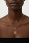 Close-up of a woman wearing a gold necklace with a square pendant on a neutral background