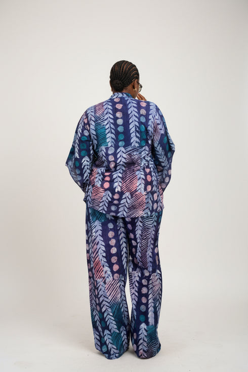 A person shown from the back wearing a long matching robe and pajama set with a colorful abstract pattern in blue, purple, pink, and white. The photo appears to be a social media or marketplace video screenshot with text overlays showing a price and WhatsApp contact, plus interface icons on the right.