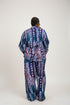 A person shown from the back wearing a long matching robe and pajama set with a colorful abstract pattern in blue, purple, pink, and white. The photo appears to be a social media or marketplace video screenshot with text overlays showing a price and WhatsApp contact, plus interface icons on the right.