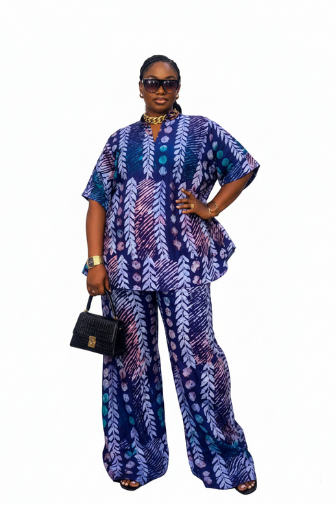 A woman modeling a matching two-piece printed outfit with a short-sleeve top and wide-leg pants in blue, purple, and white, standing in front of a black-and-white striped wall.