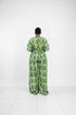A person shown from the back wearing a green and white patterned short-sleeve jumpsuit in front of a black slatted wall. Text overlays show pricing and WhatsApp contact information.