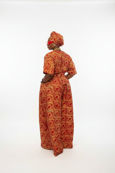 A woman wearing a red and orange patterned traditional outfit stands in front of a gray slatted wall, with overlaid text showing a price and WhatsApp contact. This is a social-media-style listing image rather than a clean product photo.