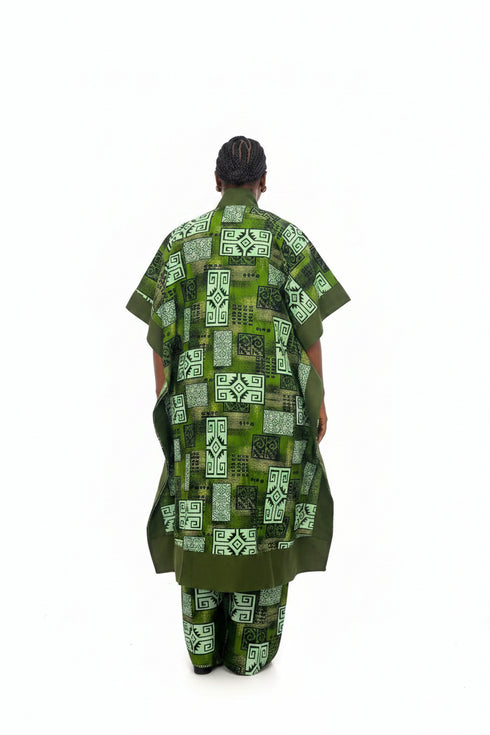 A person viewed from the back wearing a loose green patterned robe or kaftan with matching pants, photographed against a plain white studio background.