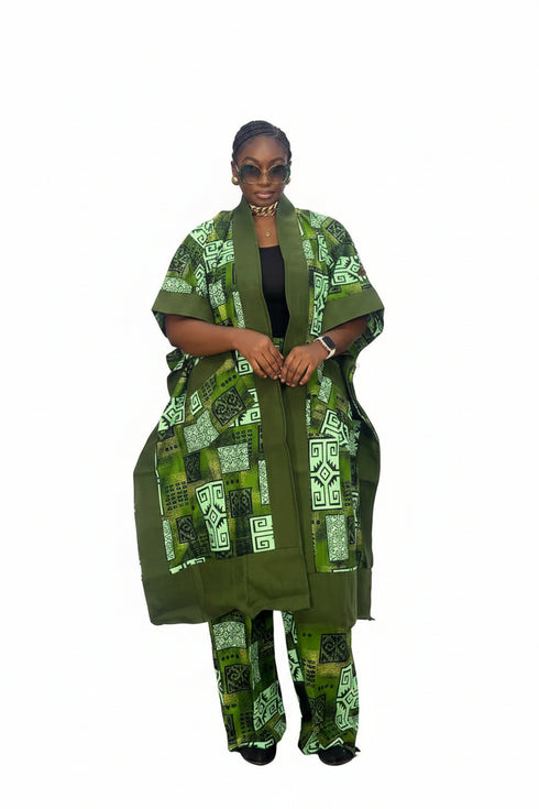 A woman modeling a green and white patterned traditional outfit consisting of a long open-front jacket, matching pants, and a black top underneath, set against a plain white background.