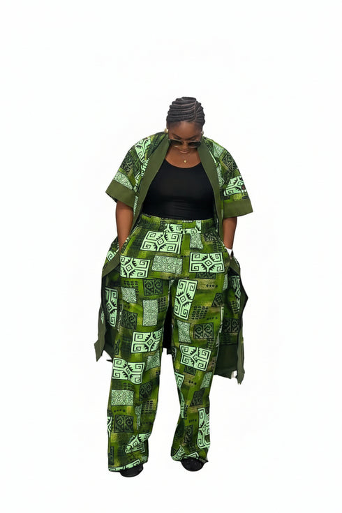 A woman modeling a green and white patterned outfit consisting of a matching jacket and wide-leg pants over a black top, standing in front of a black and white striped wall.