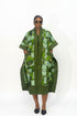 A woman modeling a green patterned kaftan dress with geometric African wax print panels, photographed against a plain white studio background.