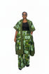 A woman modeling a green and black patterned African wax print outfit, consisting of a matching jacket and trousers with a black top underneath, set against a black and white striped background.